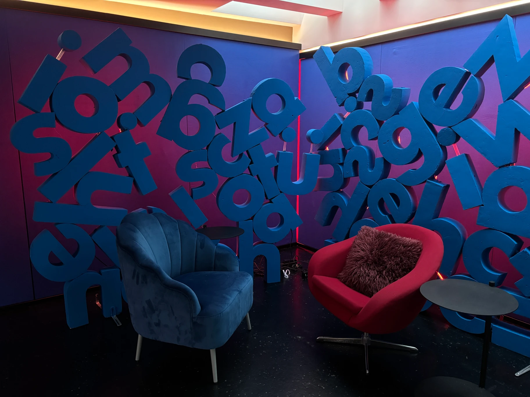 Foto des eingebauten Podcaststudios mit grossen blauen Buchstaben, farbigem Licht sowie blauem und rotem Sessel
